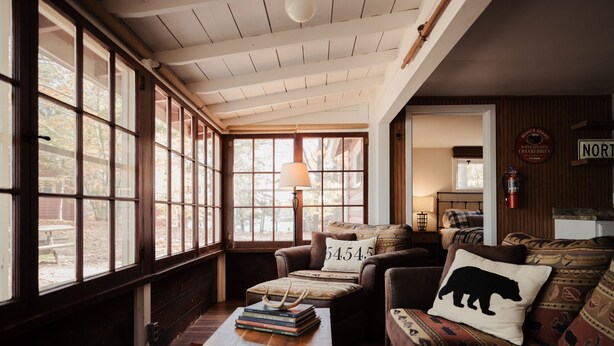 A cozy room with large windows, a wooden ceiling, a sofa with patterned cushions, and a lamp. - Relax in Bayview Cabin MW Chain, June Opening (Manitowish Waters)