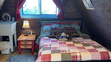 A cozy attic bedroom with a wooden floor, a bed with a quilt, a nightstand with a lamp, and a window with curtains.