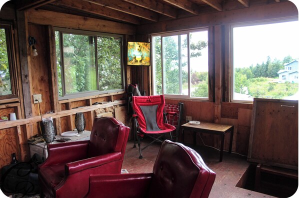 A rustic cabin interior with wooden walls, large windows, and red leather chairs.
