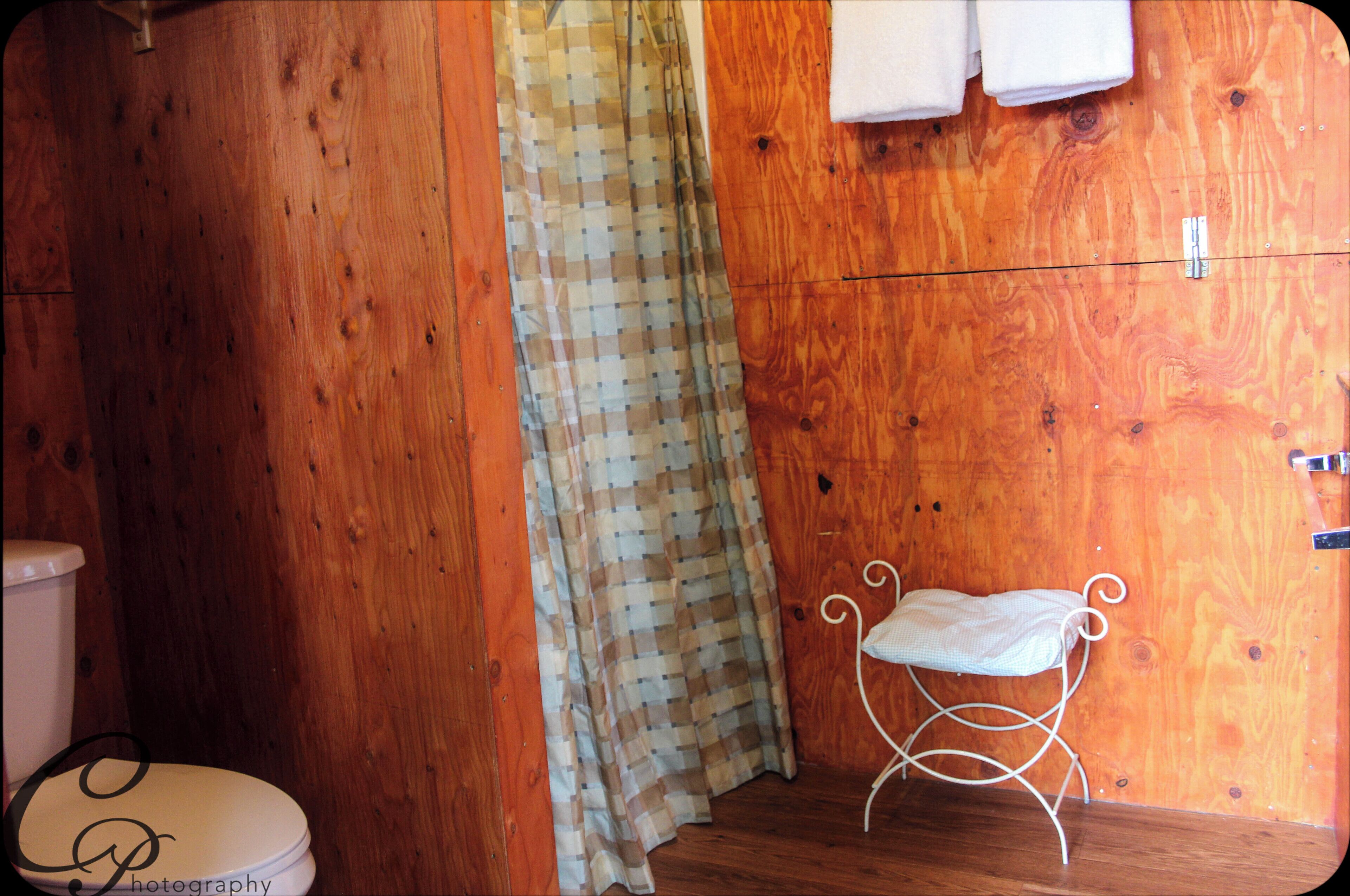 A wooden bathroom with a toilet, a shower curtain, and a small bench.