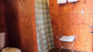 A wooden bathroom with a toilet, a shower curtain, and a small bench.