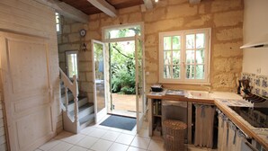 A rustic kitchen with a wooden staircase, a tiled floor, and a view of greenery outside. - Claire s' house in medieval village couze near river Dordogne with your pets (Couze)