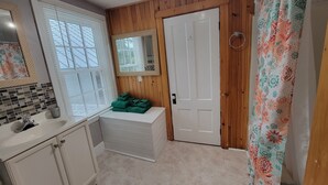 A bathroom with a sink, mirror, towel rack, and a door with a mirror above it. - The Nest - one bed apartment (Searsport)