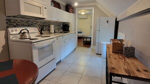A compact kitchen with white cabinets, a stove, a microwave, and a wooden dining table. - The Nest - one bed apartment (Searsport)