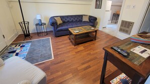 A living room with a blue sofa, a wooden coffee table, a striped armchair, a floor lamp, and a rug. - The Nest - one bed apartment (Searsport)