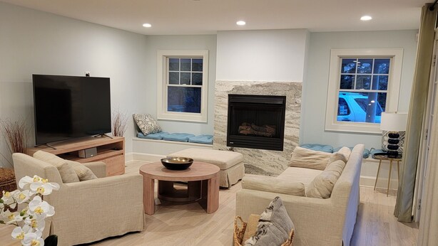 A modern living room with a flat-screen TV, a stone fireplace, and a large window. - Moments from private beach (Sag Harbor)