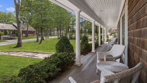 A covered porch with wicker furniture, a lawn, and trees. - Moments from private beach (Sag Harbor)