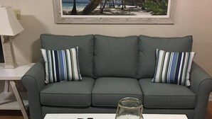 A living room with a grey sofa, striped pillows, a white coffee table, and a framed picture of a beach scene. -  40 ft to the ocean 4 bd/3 bath ocean view beach house sleeps  (Myrtle Beach)
