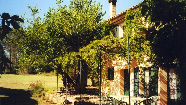 A rustic house with a stone patio, a table, and chairs outside.