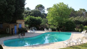 A swimming pool with a stone deck, surrounded by outdoor furniture and greenery.
