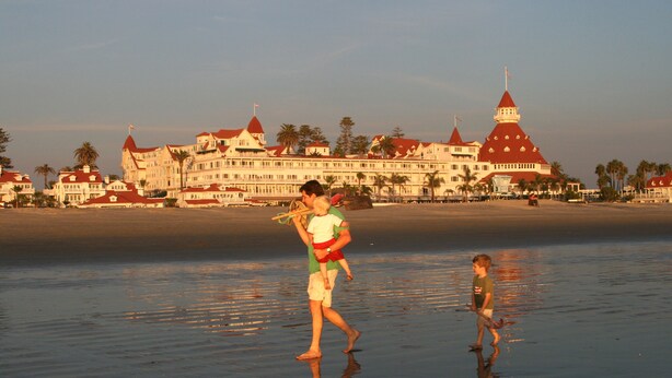 Ein Strandhotel mit mehreren Gebäuden mit roten Dächern, Palmen und einem Sandstrand.