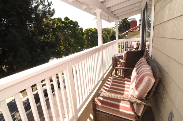 A covered porch with a wicker sofa and striped cushions, a small table, and a chair.