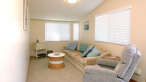 Ein Wohnzimmer mit einem beigen Sofa, zwei Beistelltischen, einem Korbtisch und einem grauen Sessel.