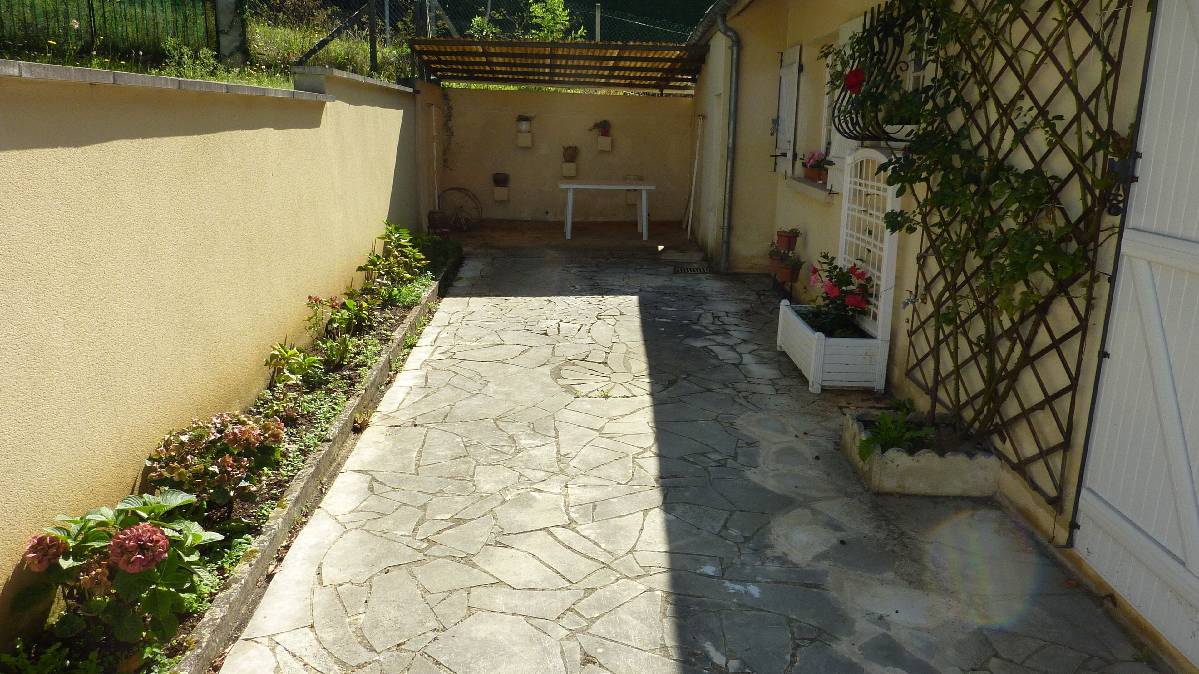 A narrow stone-paved courtyard with a white table and potted plants.
