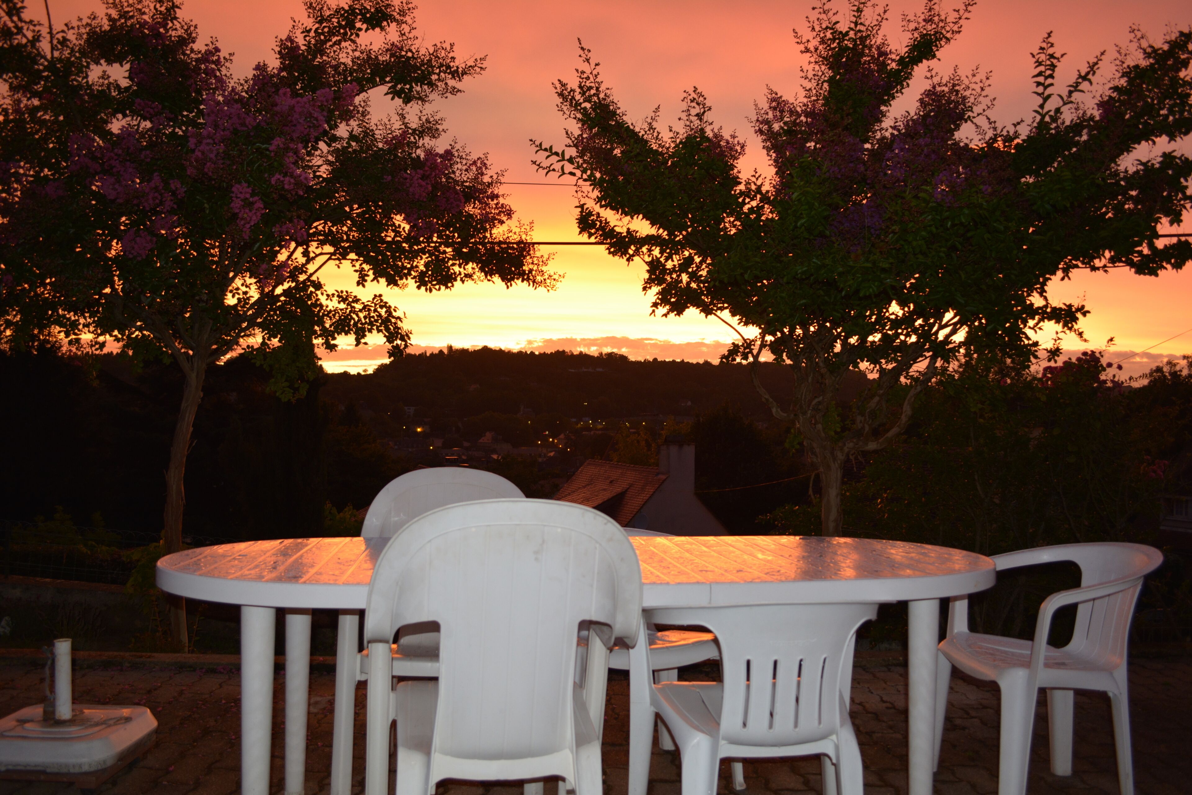 A round table with white plastic chairs, set outdoors with a sunset view.