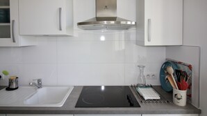 A modern kitchen with white cabinets, a stainless steel range hood, a black induction cooktop, a sink, and a dish rack with utensils. - House Bungalow 8p. any comfort near center and beaches, closed garden. St Denis (Saint-Denis-D'oléron)