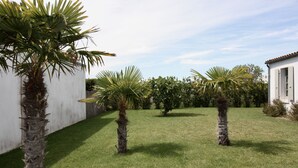 A courtyard with palm trees, a white building, and a wooden bench. - House Bungalow 8p. any comfort near center and beaches, closed garden. St Denis (Saint-Denis-D'oléron)