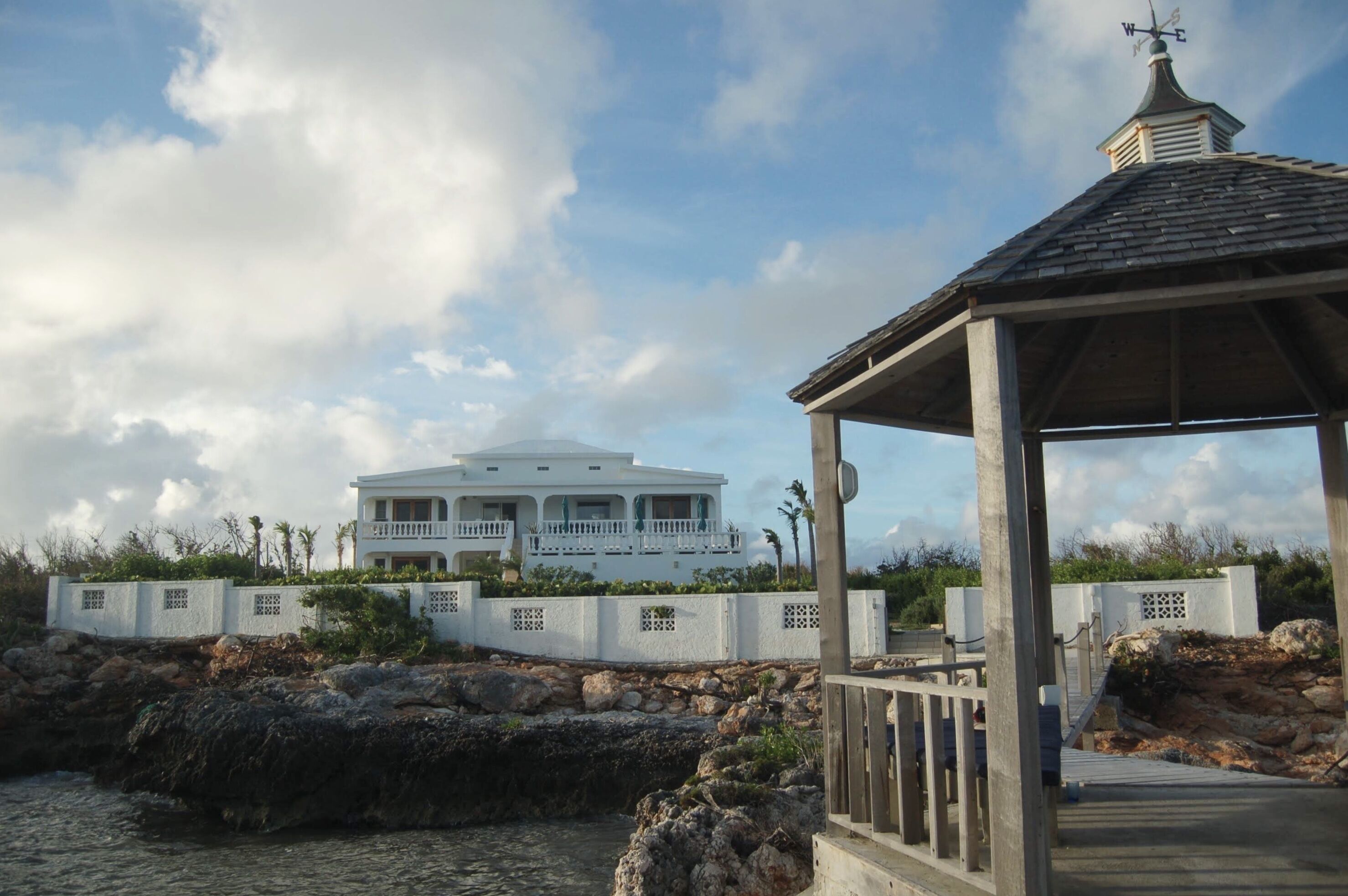 A coastal property with a large white house, a gazebo, and a rocky shoreline.