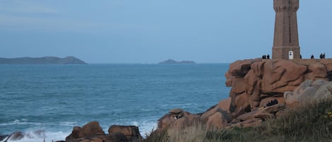 Ett kustnära fyrtorn som står på en klippig udde, med havet i förgrunden och avlägsna öar i bakgrunden.