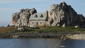A stone house with a sloped roof, situated on a rocky outcrop by a body of water. - Comfortable apartment, close to Perros-Guirec and Ploumanac'h beaches (Perros-Guirec)