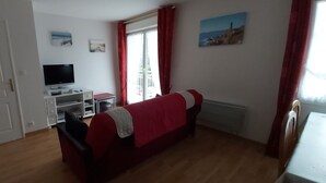 A room with a red sofa, a TV on a stand, a window with curtains, and a painting on the wall. - Comfortable apartment, close to Perros-Guirec and Ploumanac'h beaches (Perros-Guirec)