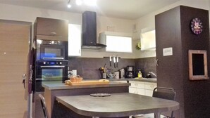 Cocina compacta con horno empotrado, microondas y un pequeño comedor con mesa y sillas.