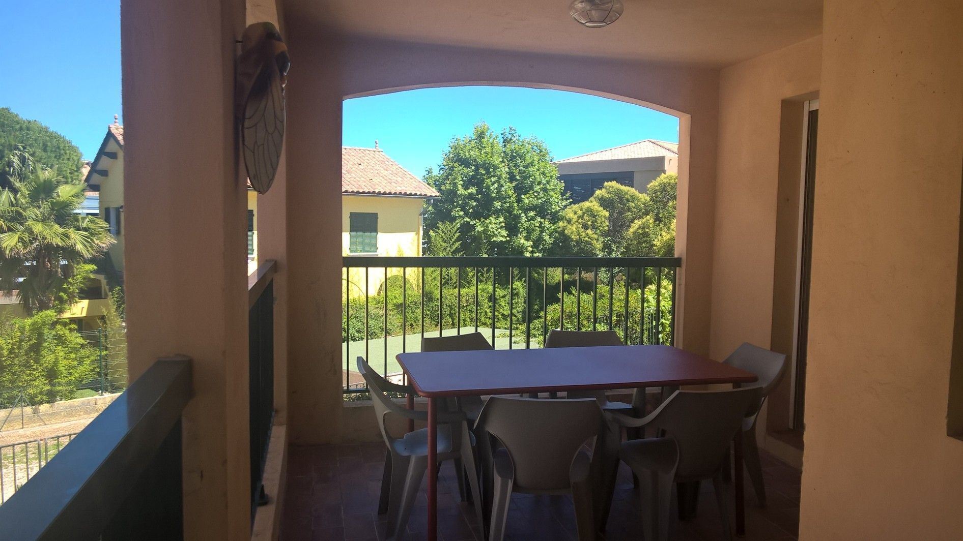 Ein Balkon mit Tisch und Stühlen, der Blick auf eine Wohngegend mit Bäumen und Häusern bietet.