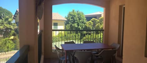 En balkon med et bord og stole, der giver udsigt over et boligområde med træer og huse.