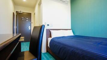 A hotel room with a bed, a desk, a chair, and an air conditioning unit on the wall.