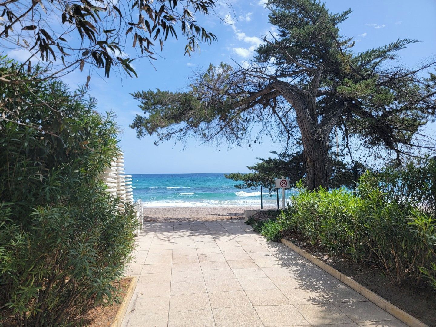 A paved pathway leading to a beach with a clear view of the ocean.
