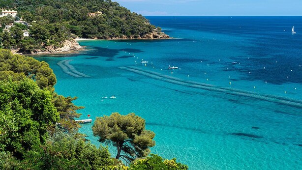 Eine Küstenlandschaft mit klarem türkisblauem Wasser, einer kleinen Insel mit dichter Vegetation und einigen Booten.