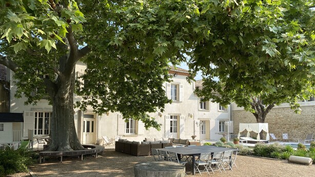 A courtyard with outdoor seating, a large tree, and a building with white shutters. - Renovated, spacious Les toiles à Elise mansion with swimming pool (Saint-Geniès-De-Comolas)
