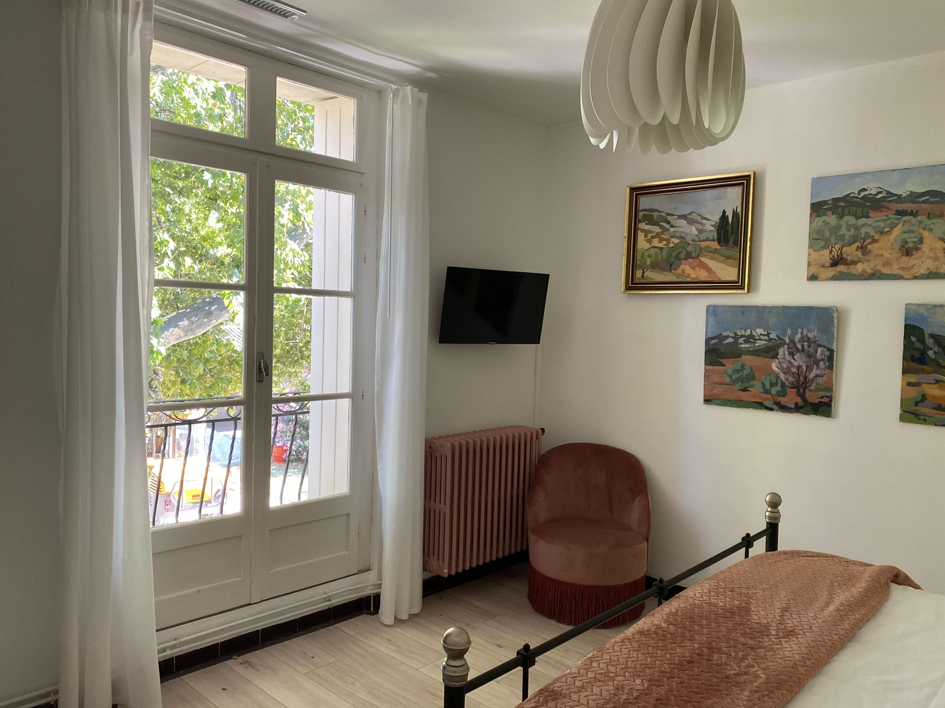 A bedroom with a bed, a chair, a radiator, a TV, and artwork on the wall.