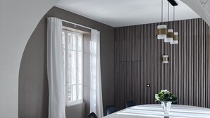 A dining area with a round table, black chairs, a white tablecloth, a vase with flowers, a window with white curtains, and a striped wall. - Renovated, spacious Les toiles à Elise mansion with swimming pool (Saint-Geniès-De-Comolas)