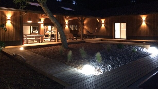 En moderne træbygning med en terrasse, swimmingpool og et spiseområde med udendørs siddepladser.