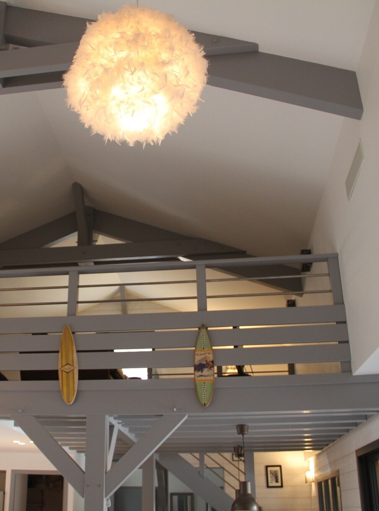 Un intérieur moderne avec un plafond haut, des poutres apparentes et un luminaire suspendu.
