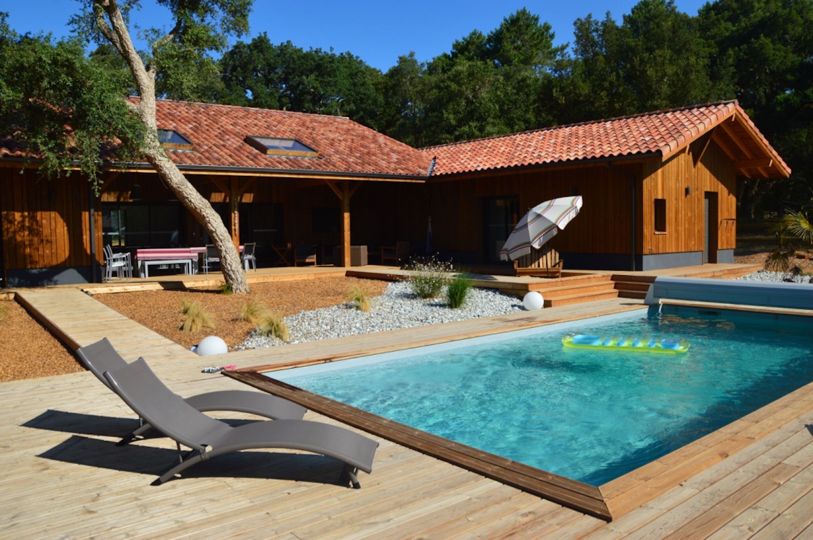 Uma cabana de madeira com piscina, espreguiçadeiras e um alpendre coberto.