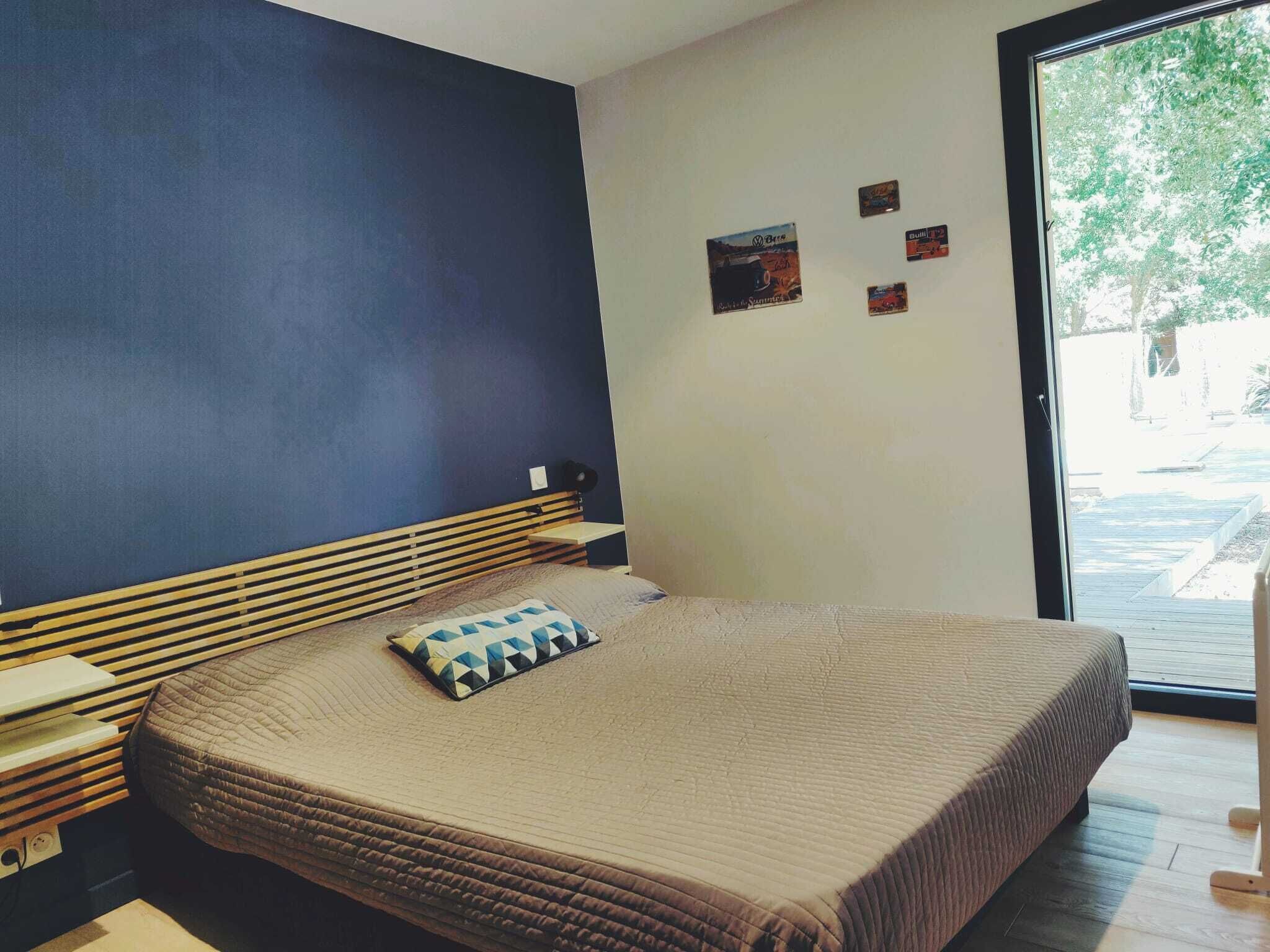 Une chambre à coucher avec un lit, une tête de lit, une fenêtre et un mur orné de petits tableaux.