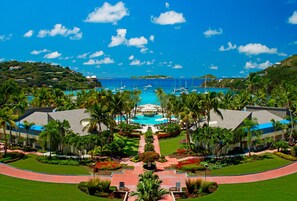 A resort with a central pool, palm trees, and a view of the ocean.