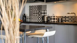 A modern kitchen with a black countertop, white chairs, and patterned backsplash tiles.