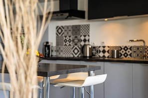 Cozinha moderna com bancada preta, cadeiras brancas e azulejos de parede estampados.