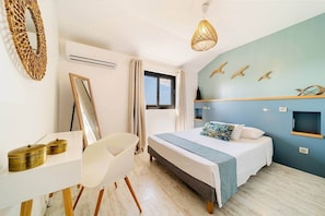 Quarto com cama, escrivaninha, cadeira, luminária pendente e parede com detalhes decorativos.