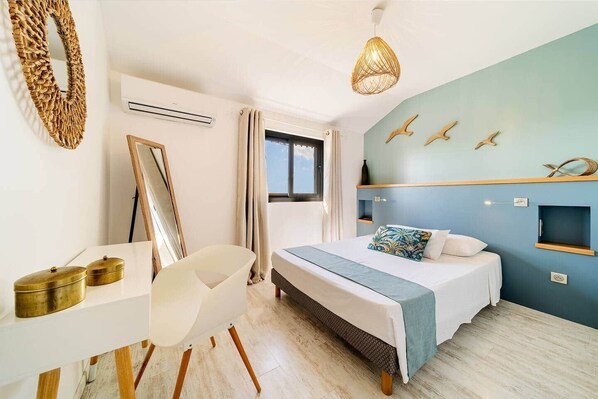 A bedroom with a bed, a desk, a chair, a hanging light fixture, and a wall with decorative elements.