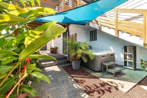 Uma área externa privativa com hidromassagem, um banco de madeira e um vaso de planta.