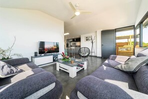 Uma sala de estar moderna com televisão de tela plana, sofás cinzas, uma mesa de centro e um ventilador de teto.