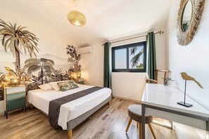 Un dormitorio con cama, mesitas de noche, escritorio, silla, ventana con cortinas y decoración en la pared.