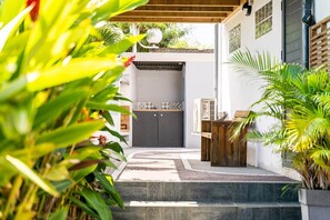 A covered outdoor area with steps leading to a door, surrounded by greenery and a tiled wall.