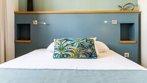 A bed with a white mattress, a teal floral pillow, and a blue headboard with two shelves.