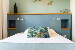 Uma cama com colchão branco, almofada floral azul-turquesa e cabeceira azul com duas prateleiras.