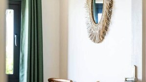 A room with a white table, a chair, a small stool, a wall-mounted mirror, and a door.